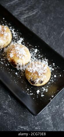 bomboloni cake or donuts with powdered sugar sprinkles and served on a black plate and stone pad Stock Photo
