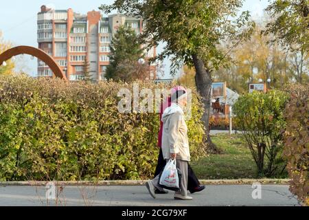 Two elderly women walk from the store along the sidewalk past a city square. Achinsk of Krasnoyarsk Region. Russia. Stock Photo