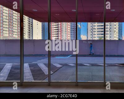 Man talks by phone and walks along the narrow sidewalk near the concrete wall around high-rise blocks building area in a new district of the city. Vie Stock Photo