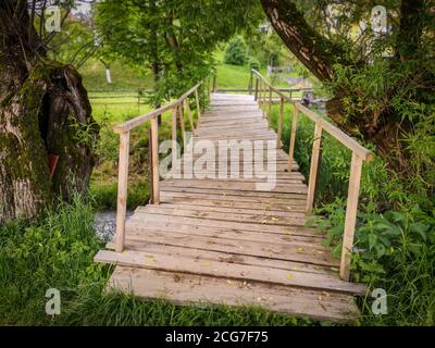 New simple wooden bridge made of planks with railings over the mountain river in a rural area. Stock Photo