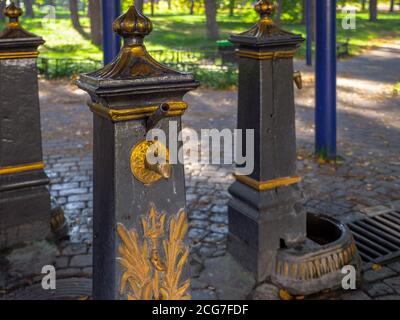 Old-fashioned public metal hand water pumps with golden decoration to draw up clean well water for people to drink and collect it in bottles. Free fre Stock Photo