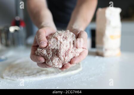 Man's hand holds minced meat over table where flour is scattered and rolled dough lies Stock Photo