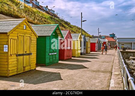 People walking past colourful beach huts on the prom at Sheringham, Norfolk, UK