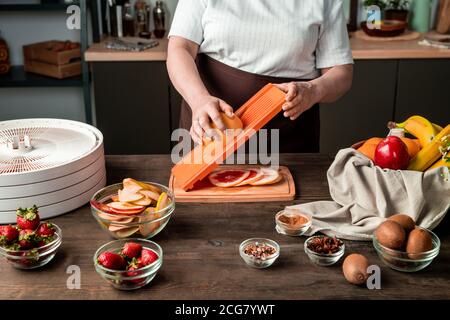 Close-up of unrecognizable woman standing at table and preparing grapefruit slices for dehydration Stock Photo