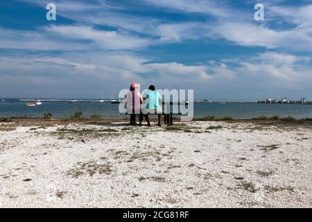 Multi-racial couple, in their forties, sitting & looking out at the water. Stock Photo
