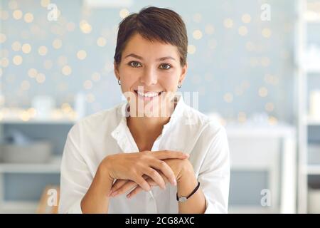 Positive woman with short haircut sitting in her home office smiling and looking at camera Stock Photo