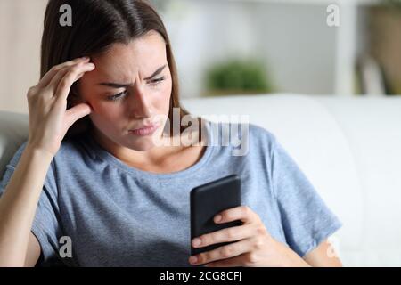 Worried girl checking smart phone sitting on a couch in the living room at home Stock Photo