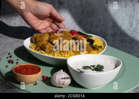 Curry plate with chilli and yogurt, food being served, hand, gray background and green plate mat Stock Photo