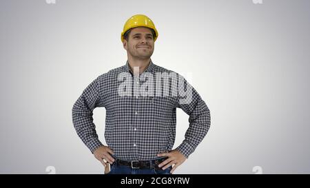 Smiling construction worker in yellow helmet looking at perfect well built object Hands on hips on gradient background. Stock Photo