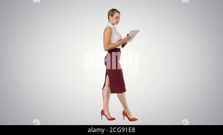 Businesswoman using electronic tab walking on gradient background. Stock Photo