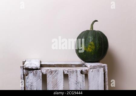 A round dark green pumpkin stands on a white wooden box on a yellow background. Copy space. Horizontal orientation. Stock Photo