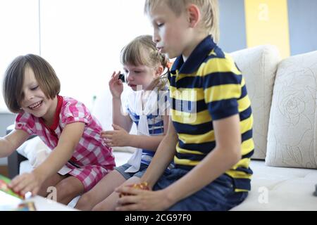 Three children play board game one girl sits and cries. Stock Photo