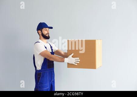 Courier holds out the box in front of him and hands it over with a smile on a gray background. Stock Photo