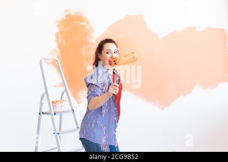 Dancing funny woman painting wall in her new apartment. Renovation and redecoration concept. Stock Photo