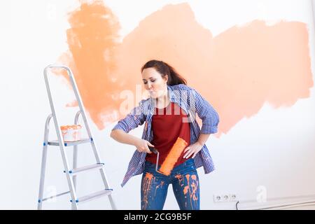 Dancing funny woman painting wall. Renovation, redecoration and repair concept. Stock Photo