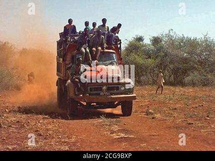 1993 - Straight on shot of a late model Isuzu dump truck loaded with Somali men.  One man rides on the right front fender while two others ride on the top of the truck's cab.  They are from the village of Maleel and are arriving at the landing zone where bags of wheat are being delivered (not shown).  This mission is in direct support of Operation Restore Hope.