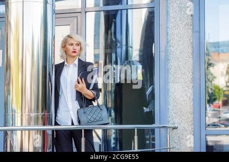 Young business woman in a black jacket near the shiny column of the business center. Stock Photo