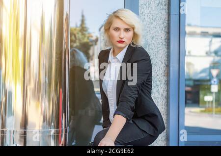 Young business woman in a black jacket near the shiny column of the business center. Stock Photo