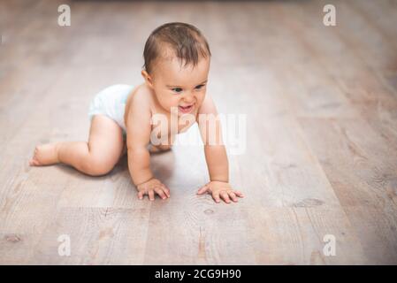 Small adorable infant standing on all fours on wooden floor at home. Stock Photo