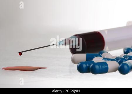 Macro view of drop of blood from syringewith pills. concept of medicine and harm to health, danger of drugs on a white background, close-up. Stock Photo