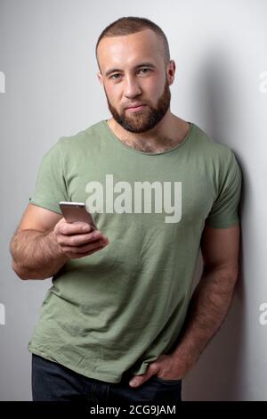 American bearded guy chatting on smart phone with friend or girlfriend, holds mobile phone, being in good mood with conversation. Stock Photo