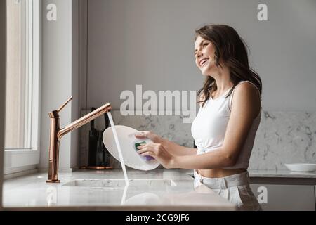 image of happy caucasian woman smiling and washing dishes in kitchen at home Stock Photo