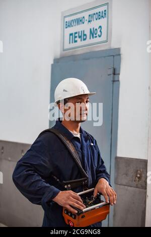 Asian worker using crane on titanium metallurgy plant. For loading titanium sponge to vacuum arc furnace. Stock Photo