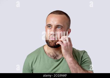 Caucasian adult pencive man with beard thinking doubting and pondering, working out decision, keeping hand near his chin and looking aside, isolated o Stock Photo