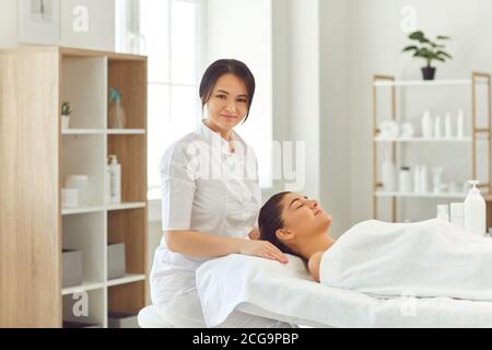 Smiling woman dermatologist sitting near relaxing woman client and preparing for skincare treatment Stock Photo