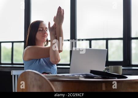 woman with her crossed arms doing yoga exercise resting during working day. Stock Photo