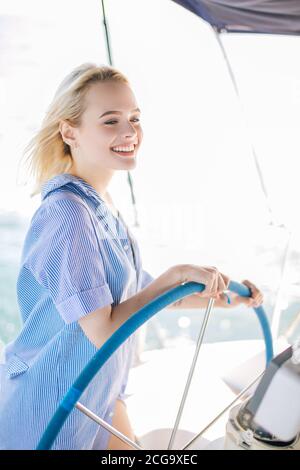 Attractive blonde woman behind the wheel yacht, enjoying sea nature and freedom, active sailor girl, female driving luxury water transport, summer vac Stock Photo