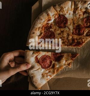 A large round juicy mouth-watering pizza with cheese and salami lies on a cardboard box from a delivery package. paper backing. close view. see flour.