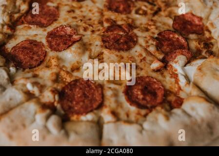 A large round juicy mouth-watering pizza with cheese and salami lies on a cardboard box from a delivery package. paper backing. close view. see flour. Stock Photo
