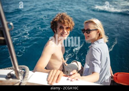 Loving happy caucasian couple on sailing boat feed looking at camera, view from th back. Redhead Hipster with his girlfriend enjoying sea vacation tri Stock Photo