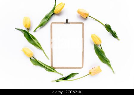 Clipboard mock up with beautiful yellow tulips isolated on white background. Flat lay, top view. Minimalistic office desk. Beauty blog concept. Stock Photo