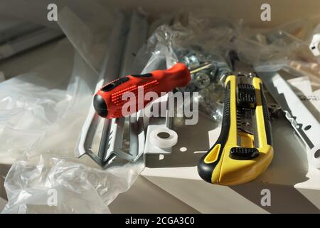 Close up view on paper cutter with yellow black plastic handle and snap off utility blade and red screwdriver together with dismantled part of drawer. Stock Photo