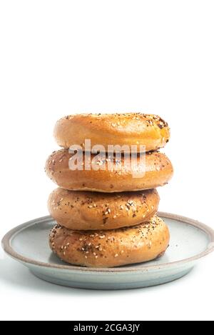 A single tall stack of four freshly baked bagels on a ceramic plate set on a plain white background. Stock Photo