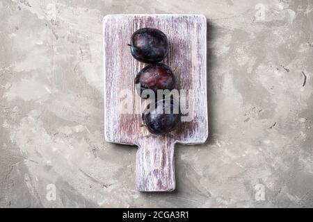 Fresh ripe plum fruits on wooden cutting board, stone concrete background, top view Stock Photo