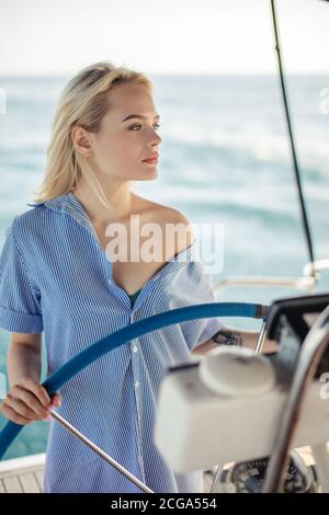 Attractive blonde woman behind the wheel yacht, enjoying sea nature and freedom, active sailor girl, female driving luxury water transport, summer vac Stock Photo