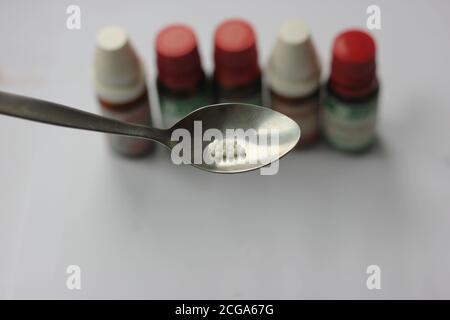 Homeopathic globules on spoon, background homeopathic bottles blurred. Stock Photo