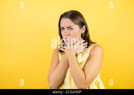 Young beautiful woman over isolated yellow background touching painful neck, sore throat for flu, clod and infection Stock Photo