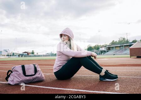 woman sat on a running track with a sports bag waiting Stock Photo