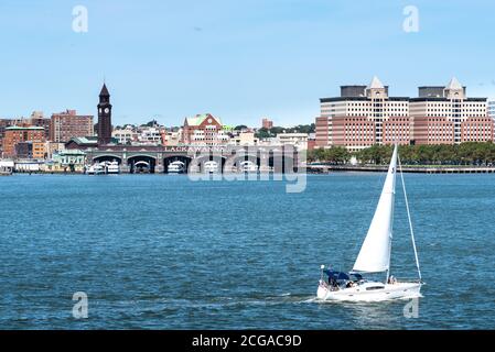 Hoboken, NJ USA - AUGUST 26 2020: A small sailboat on the Hudson River. Across the river is the historic Erie-Lackawanna Ferry Terminal in Hoboken, NJ Stock Photo