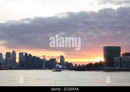 warm sun rays break through thick and dark sunset Clouds over Canary Wharf skyline, River Thames  East London England Stock Photo
