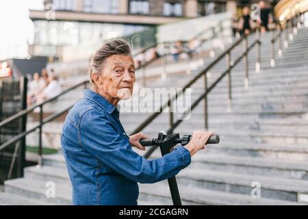 90 year old woman with gray hair, wrinkles, progressive and active uses modern electric transport scooter. Lady pensioner use eco friendly city Stock Photo