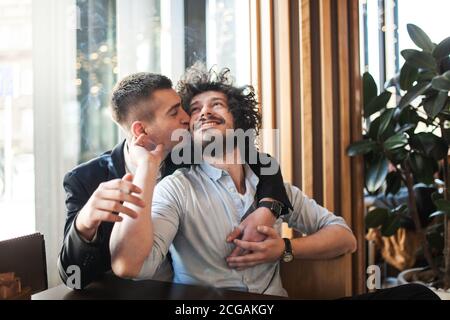 Two male friends in a cafe hugging and kissing on the cheek Stock Photo