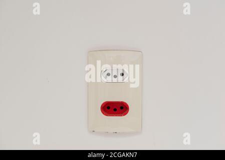 Close Up shot of a white wall plug with a Swiss and Brazilian standard socket. 3-pin socket. White socket (127 volts) and red socket (220 volts). Sock Stock Photo
