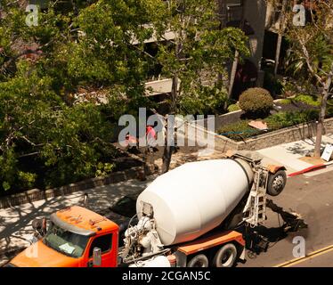 Cement mixer truck and workers laying concrete for driveway. Overhead view of truck, workers, city street, and apartment building in San Diego, Calif. Stock Photo