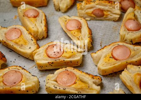Baking Bun with Sausage and mustard puff pastry rolls. Delicious snacks, tapas, breakfast, appetizers on baking paper. Top view. Close-up Stock Photo
