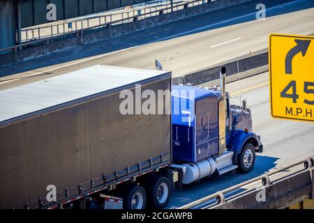 Bright blue industrial diesel long haul classic big rig semi truck tractor transporting commercial cargo in covered semi trailer with frame driving on Stock Photo